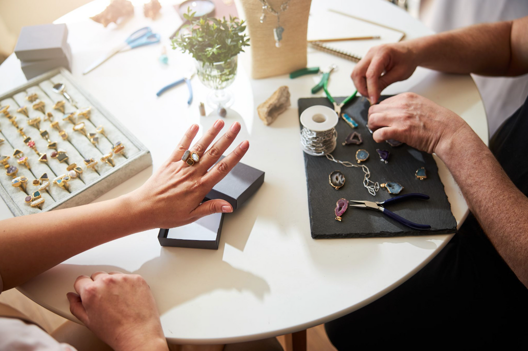 Jeweler working on handcrafted gemstone jewelry while client tries on a unique designer ring